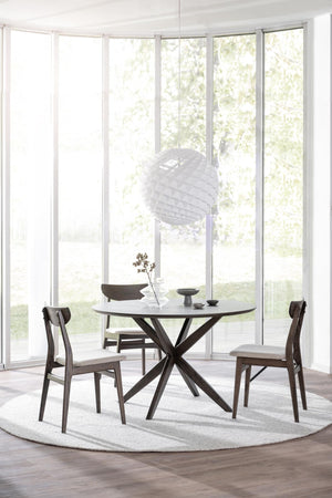 Runt matbord i mörkt trä med korsben och stoppade stolar i modern matsal med stora fönster