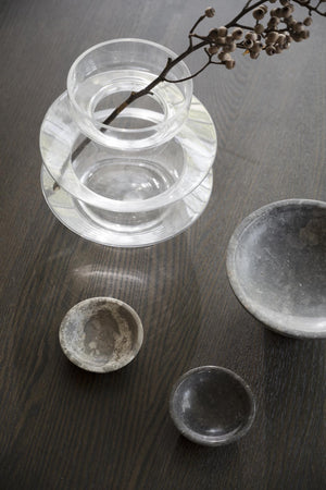 Glasvas med bred öppning och dekorativa cementfat på träbord med torkad kvist