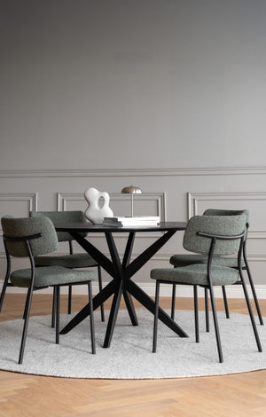 Matgrupp med runt bord i svart och gröna stolar på rund matta i ljus matsal med tavellist