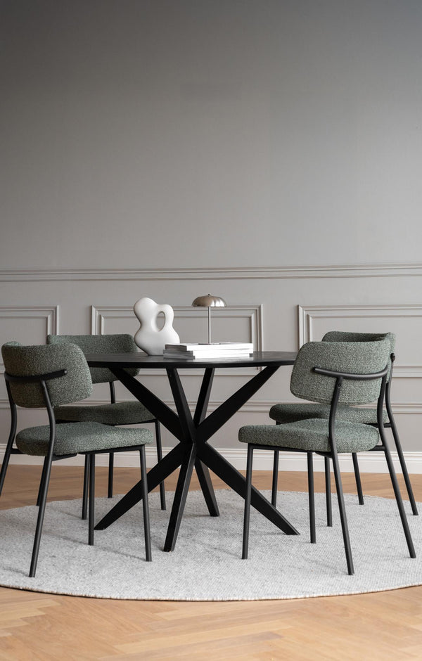 Matgrupp med runt bord i svart och gröna stolar på rund matta i ljus matsal med tavellist