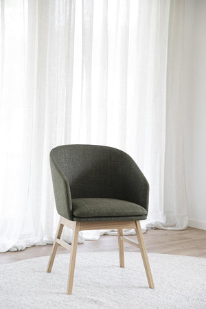Grön matstol med träben i ljust trä framför vita gardiner på trägolv