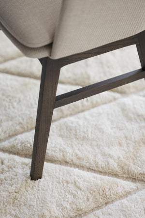 Närbild på mörkbruna träben från fåtölj med beige klädsel på vit luggmatta