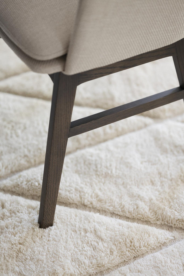 Närbild på mörkbruna träben från fåtölj med beige klädsel på vit luggmatta