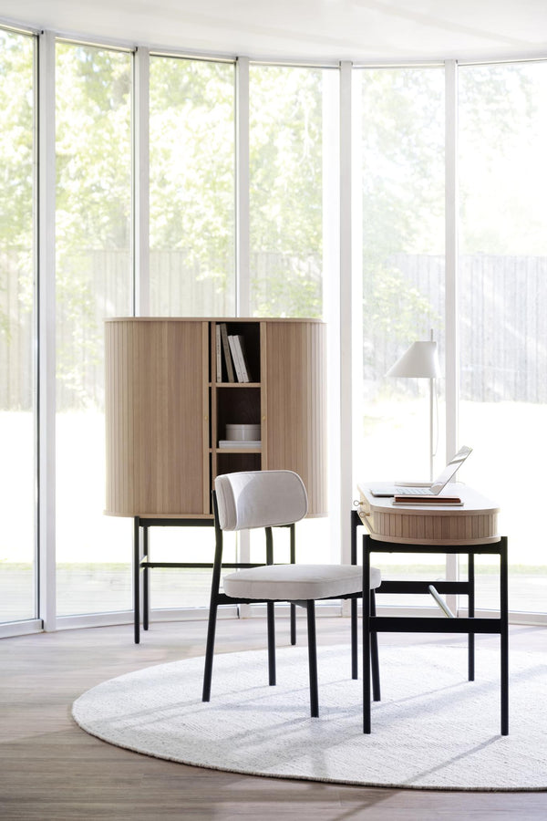 Ljust arbetsrum med skrivbord, stol och skåp i ek och svart metall framför stora fönster med trädgårdsvy