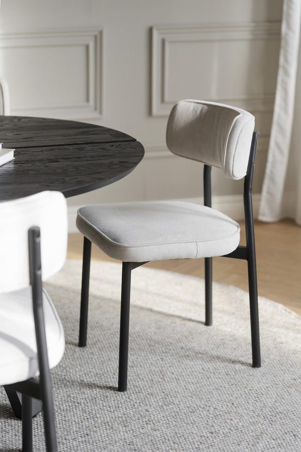 Matstol med grå tygklädsel och svarta ben vid runt matbord i modern skandinavisk stil