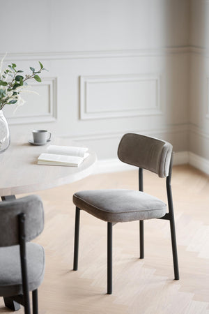 Grå stoppad matstol med svarta ben vid vitt runt matbord i ljust minimalistiskt rum