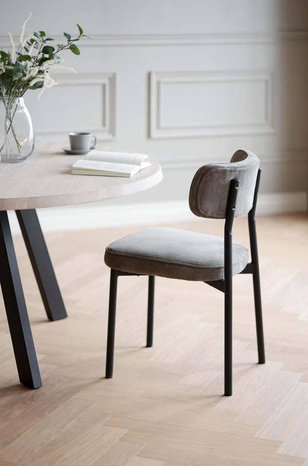 Grå stol med svarta ben vid runt matbord i ljus skandinavisk matsal med parkettgolv