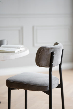 Grå stoppad stol med svarta ben vid matbord i minimalistisk skandinavisk stil