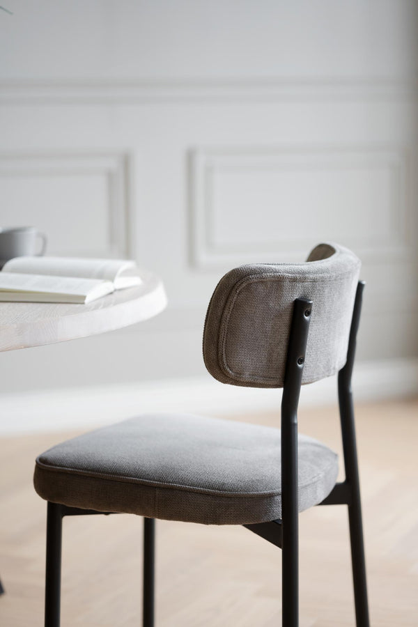 Grå stoppad stol med svarta ben vid matbord i minimalistisk skandinavisk stil