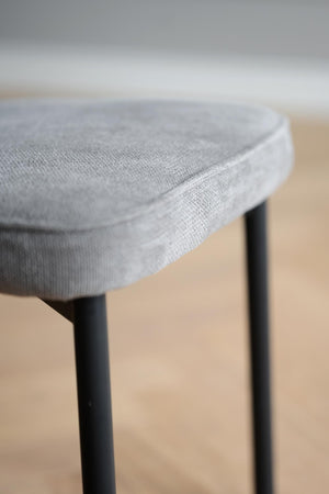 Grå stoppad pall med tyg och svarta ben i närbild