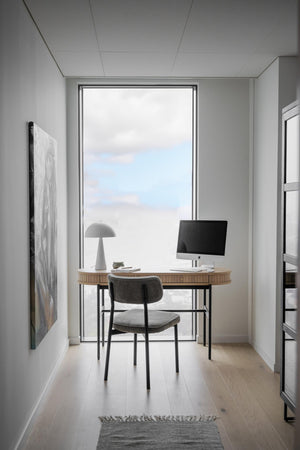Minimalistiskt hemmakontor med skrivbord i ljust trä, grå stol och datorskärm framför stort fönster