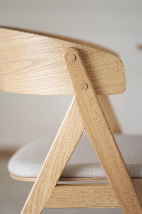 Närbild på träpall i ljus ek med synliga träfibrer och skruvdetaljer, stapelbar design med textilkudde