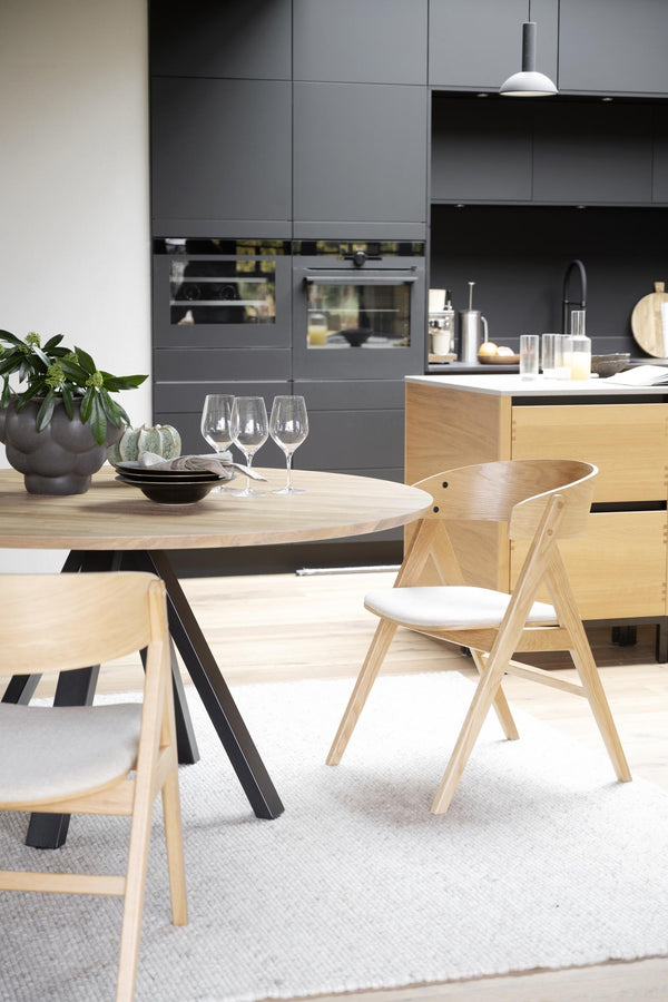 Modern matgrupp med runt bord i ljust trä och matchande stolar i skandinavisk design mot grått kök