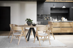 Modern matgrupp med runt bord och ljusa trästolar i skandinavisk köksmiljö med grå skåp
