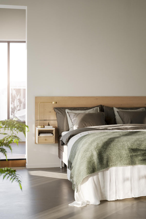 Ljust sovrum med säng i naturligt trä, gröna och grå textilier, växtdekorationer och minimalistisk inredning