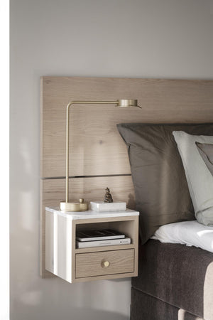 Väggmonterat nattduksbord i vit marmor och ljust trä med mässinglampa vid säng med grå sängkläder