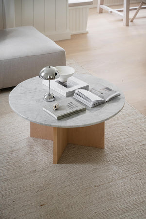 Runt soffbord med vit marmorskiva och träunderrede, dekorerat med böcker och lampa i ljust vardagsrum