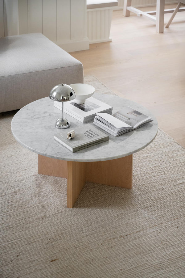 Runt soffbord med vit marmorskiva och träunderrede, dekorerat med böcker och lampa i ljust vardagsrum