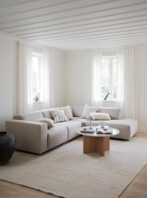 Ljust vardagsrum med beige modulsoffa, rund soffbord i trä och matta i naturliga toner