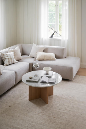 Ljust vardagsrum med beige modulsoffa, runt marmorbord med träben och textilmatta i naturliga toner