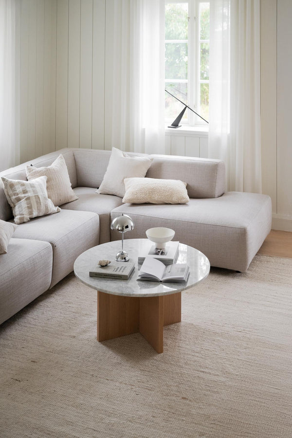 Ljust vardagsrum med beige modulsoffa, runt marmorbord med träben och textilmatta i naturliga toner
