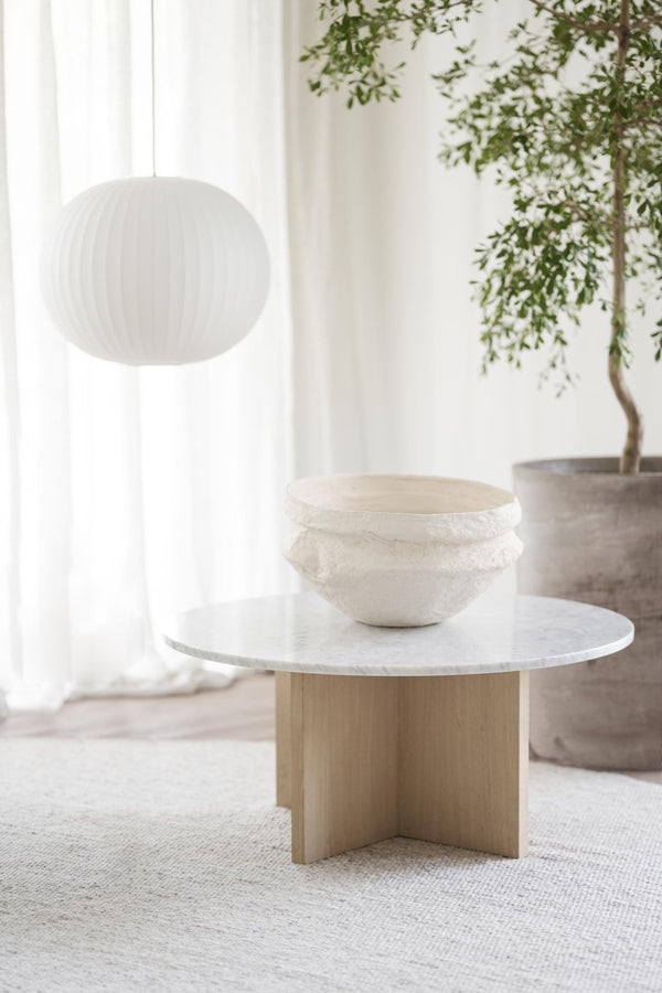 Runt soffbord med vit marmorskiva och träfot i korsform, med vit skål och grön växt i ljust rum