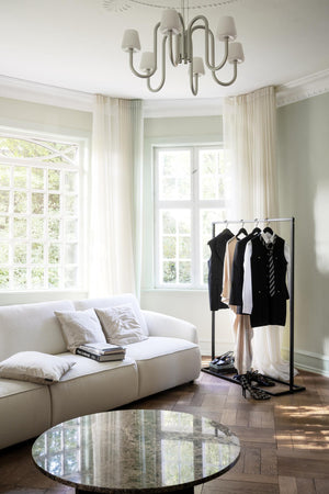 Elegant vardagsrum med vit soffa, klädställning i svart metall och rund spegelbord under modern taklampa