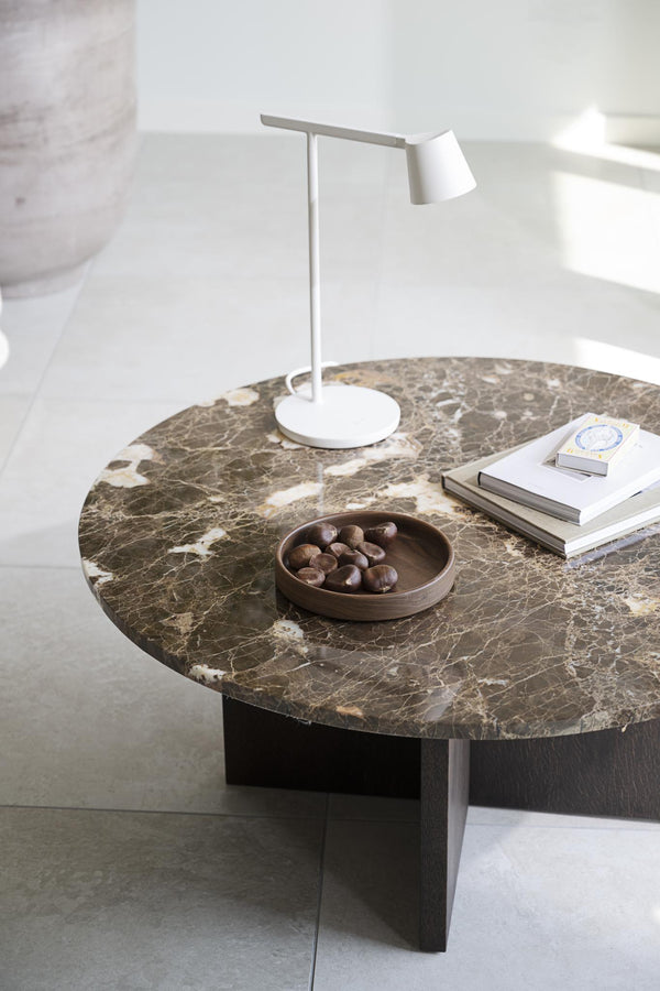 Runt soffbord med brun marmorskiva och svart träben, dekorerat med lampa, böcker och skål med choklad