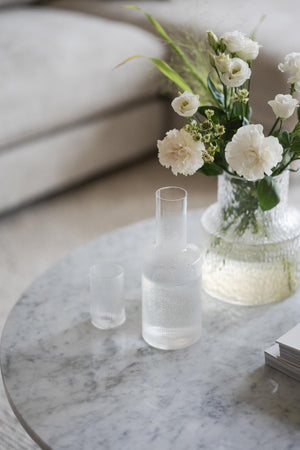 Genomskinlig sprayflaska på marmorbord med vit blombukett i bakgrunden