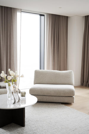 Ljust vardagsrum med beige fåtölj, långa gardiner och stort fönster i minimalistisk skandinavisk stil