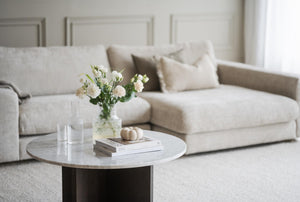 Ljust vardagsrum med beige soffa, marmorbord, vita blommor och minimalistisk inredning i neutrala toner