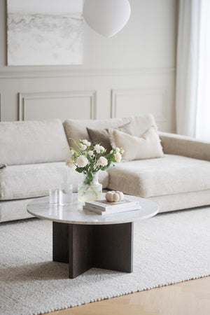 Runt soffbord med marmortop och mörkbrun träfot framför beige soffa i minimalistisk vardagsrumsinredning