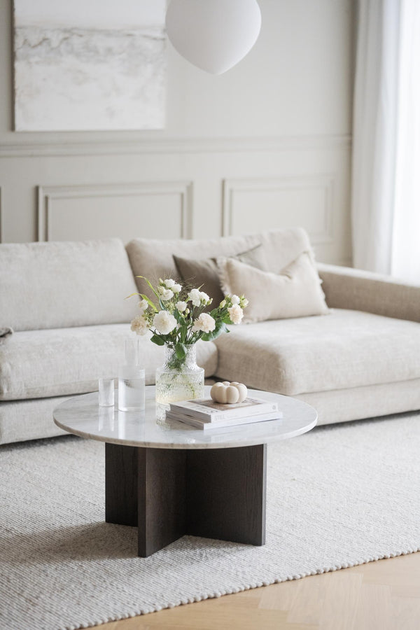 Runt soffbord med marmortop och mörkbrun träfot framför beige soffa i minimalistisk vardagsrumsinredning