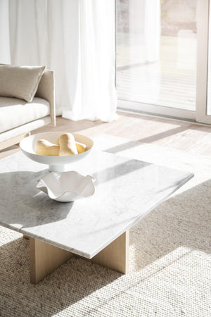 Vitt soffbord i marmor med träben och dekorativa skålar i minimalistiskt vardagsrum med ljusinsläpp