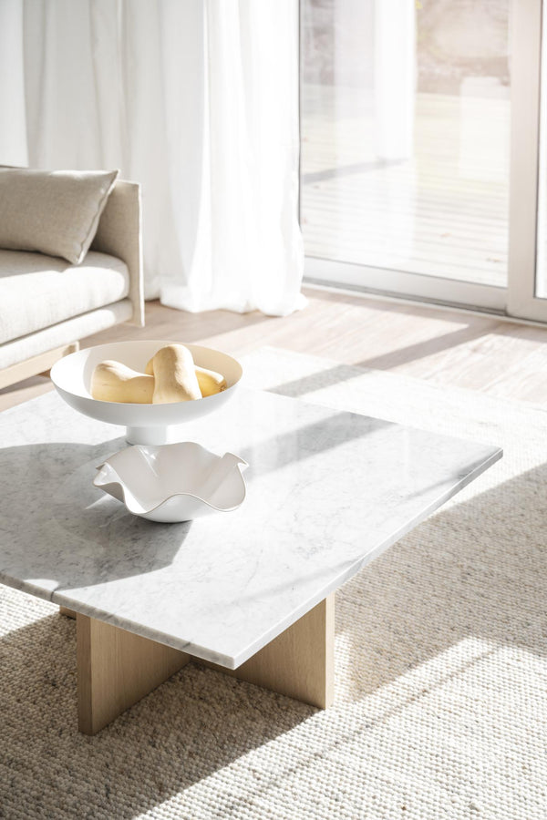 Vitt soffbord i marmor med träben och dekorativa skålar i minimalistiskt vardagsrum med ljusinsläpp