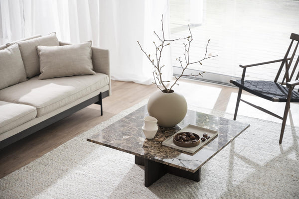 Minimalistiskt vardagsrum med beige soffa, marmorbord och svart stol i skandinavisk stil