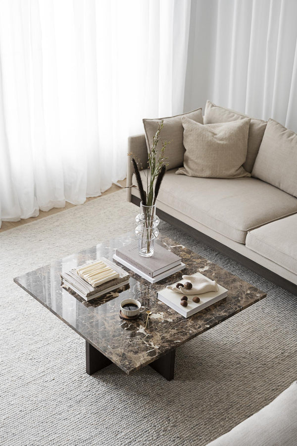 Modernt soffbord i marmor med böcker, vas och dekorativa objekt framför beige soffa med kuddar