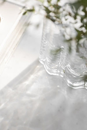 Glasfat med vågig kant och dekorativa detaljer på marmorunderlägg med grönska i bakgrunden