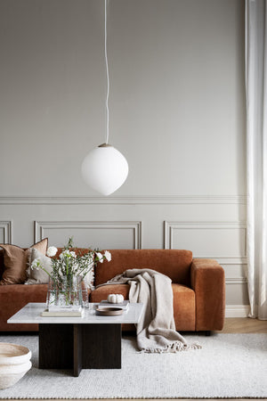 Vardagsrum med orange sammetssoffa, vit klotformad taklampa och modern soffbord i marmor och trä