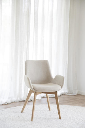Beige stol med träben i modern skandinavisk design framför vita gardiner