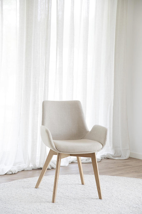 Beige stol med träben i modern skandinavisk design framför vita gardiner