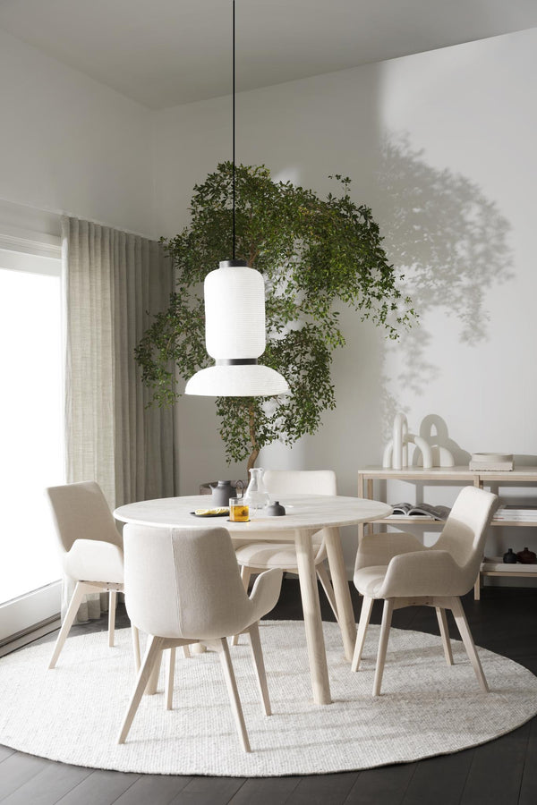 Minimalistisk matplats med runt vitt bord, beiga stolar och modern taklampa under grönt träd