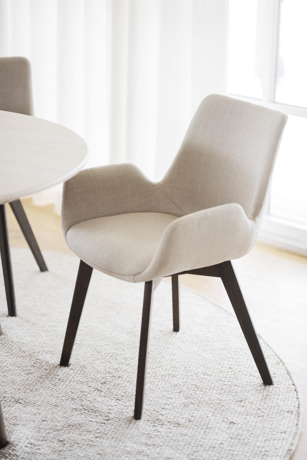 Beige stoppad stol med armstöd och mörkbruna träben i modern skandinavisk design