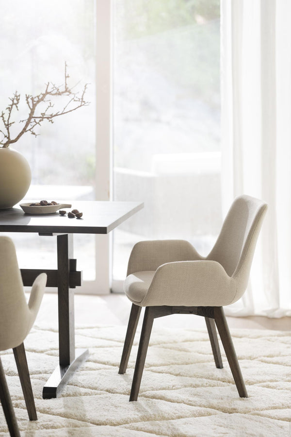 Beige matstol med armstöd och mörka träben vid matbord i ljust och minimalistiskt matrum