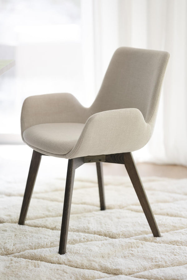 Beige stoppad stol med armstöd och mörka träben på ljus matta i modernt rum