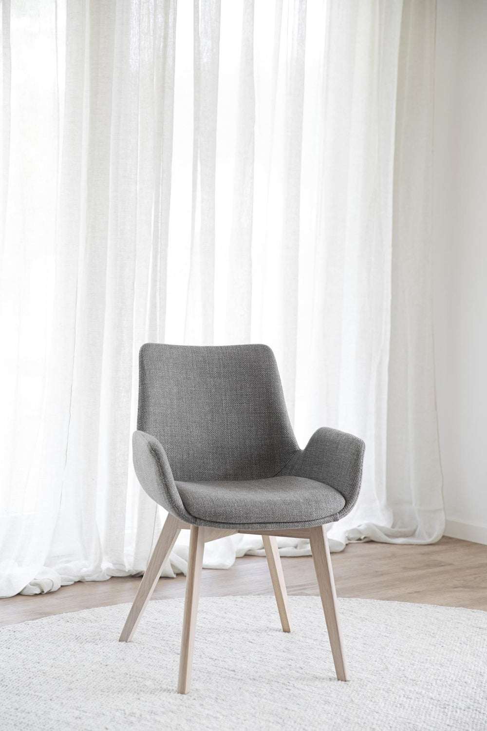 Grå fåtölj med armstöd och ljusa träben i modern skandinavisk design