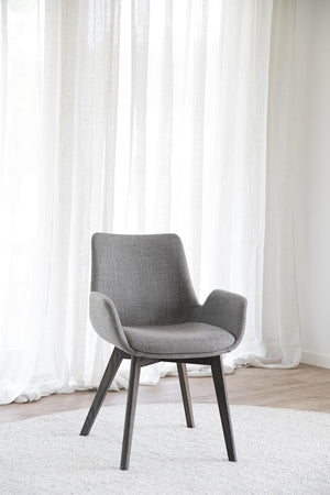 Grå matstol med armstöd och svarta ben framför vita gardiner i ljust rum