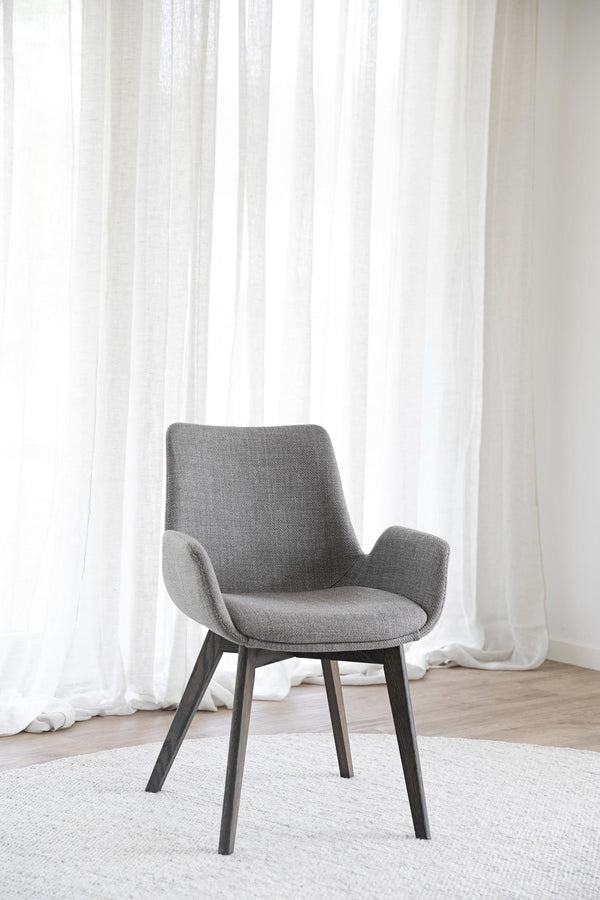 Grå matstol med armstöd och svarta ben framför vita gardiner i ljust rum