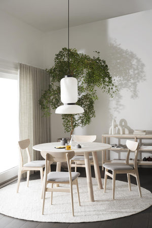 Ljus matplats med runt bord, trässtolar och vit taklampa under gröna växter i minimalistisk skandinavisk stil