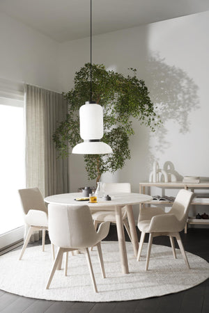 Minimalistisk matplats med runt vitt bord, beiga stolar och modern taklampa under gröna växter